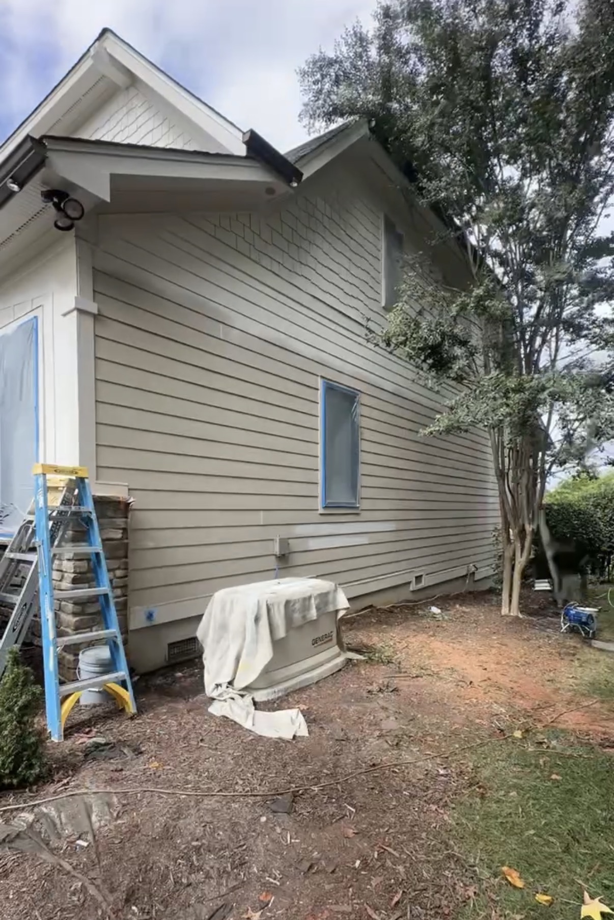 Side of the home mid-repaint with protected windows and covered equipment